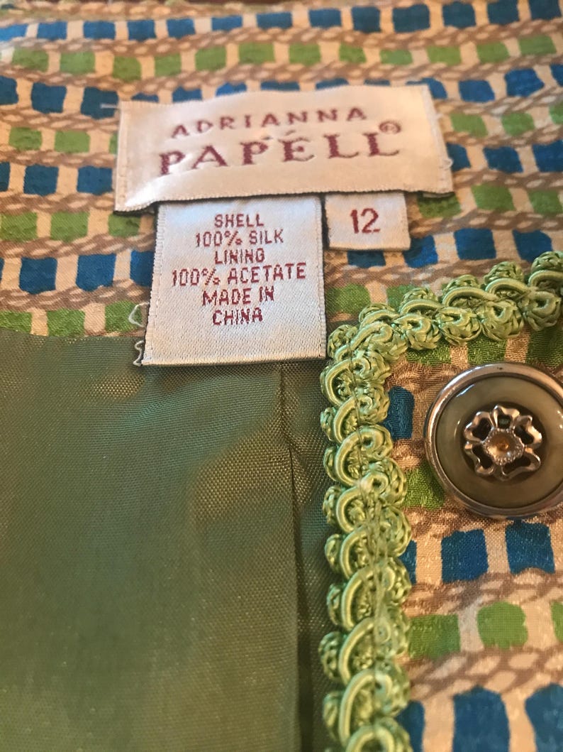 May include: A green and brown patterned fabric with a green trim and a green button. The fabric has a label that reads "Adrianna Papell" and "Shell 100% Silk Lining 100% Acetate Made in China" and a size tag that reads "12".