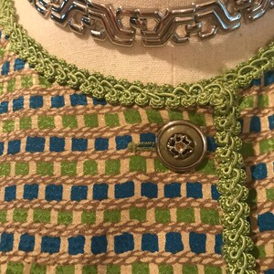 May include: A close-up of a green and blue patterned fabric with a silver chain necklace and a green button.