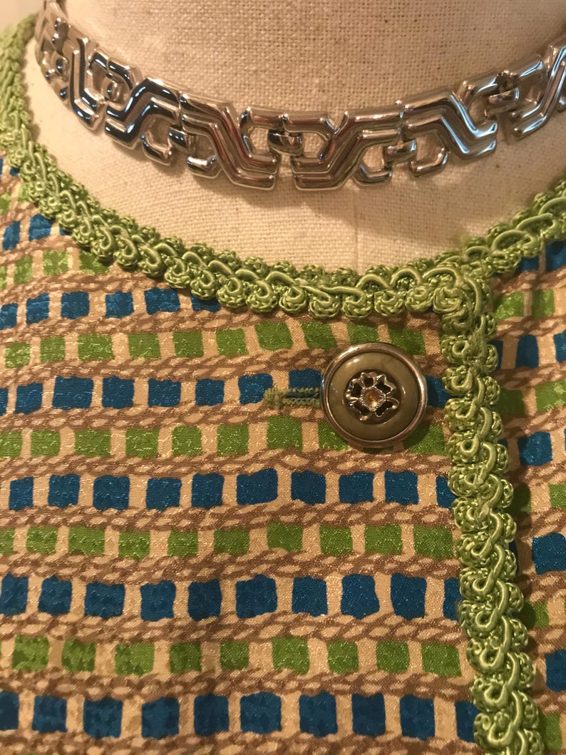 May include: A close-up of a green and blue patterned fabric with a silver chain necklace and a green button.