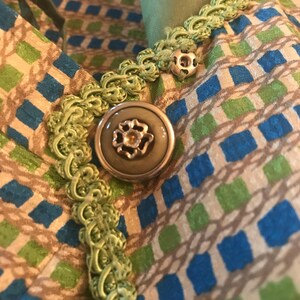 May include: A close-up of a green and brown fabric with a green trim and a large, round, silver button with a floral design.