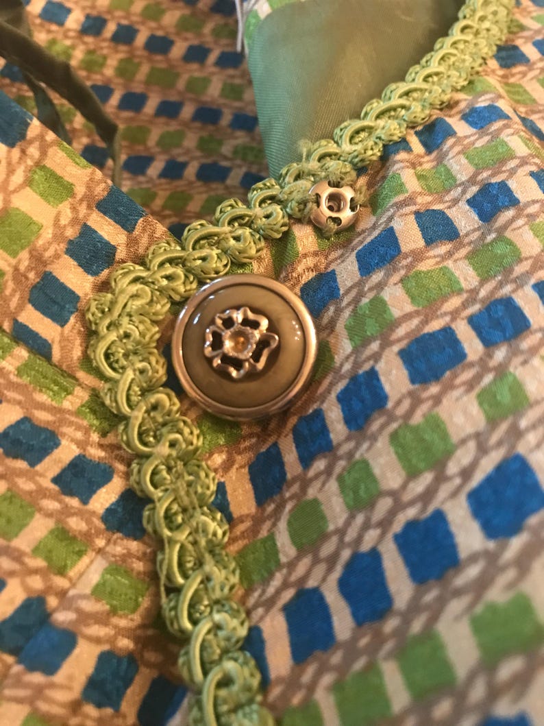May include: A close-up of a green and brown fabric with a green trim and a large, round, silver button with a floral design.