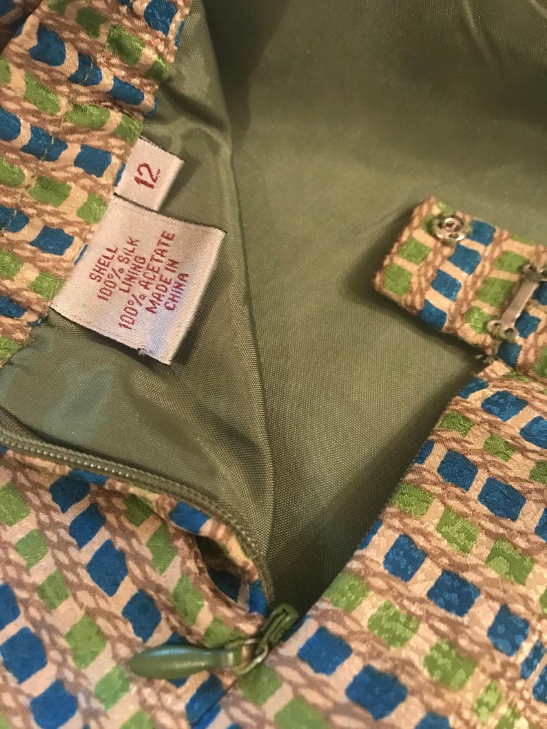 May include: A green, blue, and brown patterned dress with a zipper closure. The dress has a tag that reads "Shell 100% Silk Lining 100% Acetate Made in China" and a size tag that reads "12".