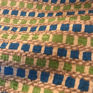 May include: A close-up of a fabric with a repeating pattern of blue, green, and brown squares. The fabric has a subtle texture and a slightly iridescent sheen.