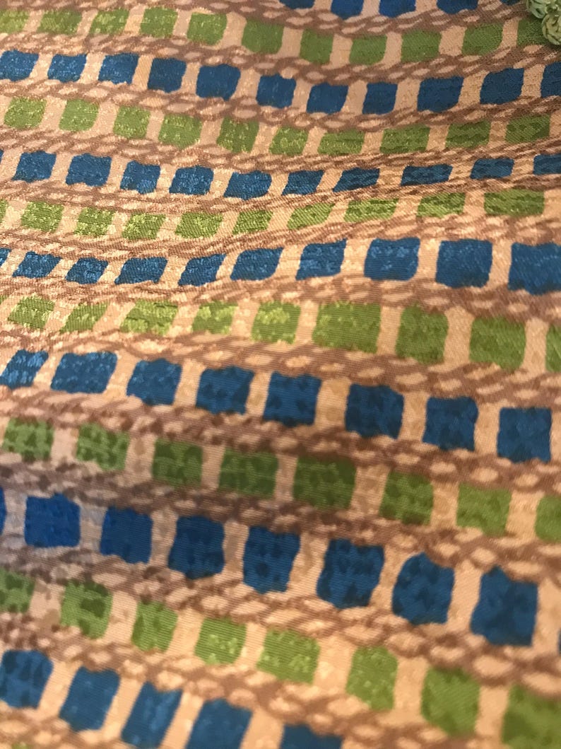 May include: A close-up of a fabric with a repeating pattern of blue, green, and brown squares. The fabric has a subtle texture and a slightly iridescent sheen.