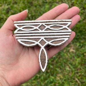 May include: A brown wooden block printing stamp with a white geometric design. The design features a series of interlocking circles and lines.