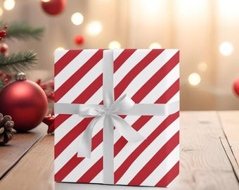 Puede incluir: Una caja de regalo a rayas rojas y blancas con una cinta de satén blanca atada en un lazo. La caja está sobre una superficie de madera.