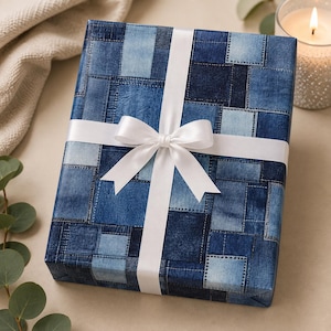 May include: A rectangular gift box wrapped in paper featuring a blue denim patchwork pattern with various shades of indigo and light blue squares. The package is tied with a smooth, white satin ribbon that is knotted into a centered bow.