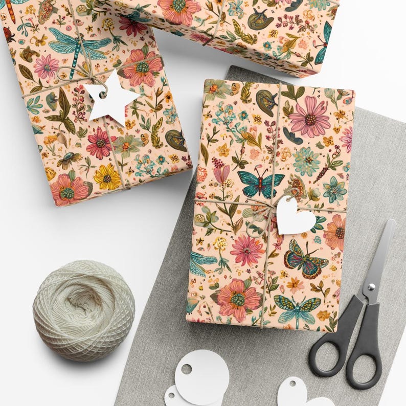 May include: Three wrapped gifts with floral patterned paper featuring butterflies, dragonflies, and flowers in pink, blue, and yellow. Each gift is tied with twine and a white tag. A ball of twine, scissors, and blank tags are also present.