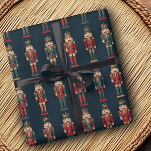 May include: Gift wrap featuring a repeating pattern of toy nutcrackers in red, green, and gold on a dark blue background. A black ribbon is tied around the wrapped package, creating a festive presentation.