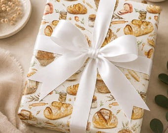 May include: A rectangular gift box wrapped in cream-colored paper featuring a repeating watercolor pattern of various artisan breads, woven baskets, rolling pins, and flour sacks, tied with a wide, smooth, white satin ribbon bow.