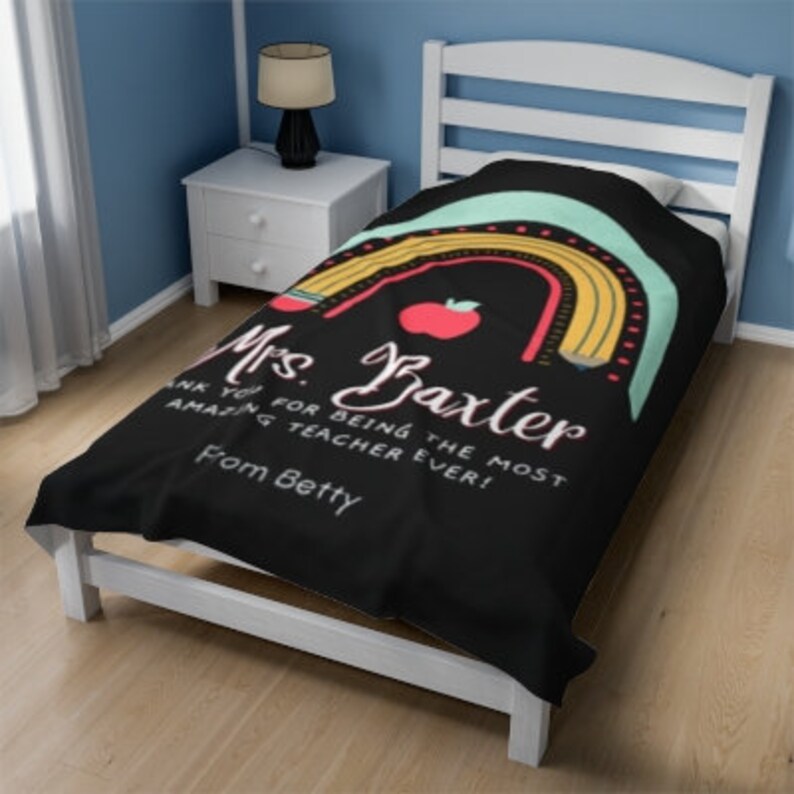 May include: Black twin-sized bedspread with a rainbow design featuring pencils and an apple. The text reads "Mrs. Baxter Thank you for being the most amazing teacher ever! From Betty".