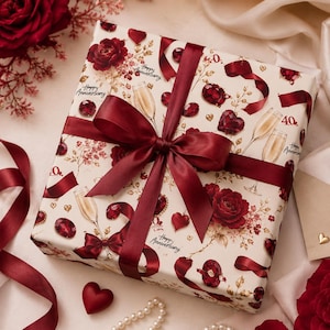 May include: A wrapped gift with a burgundy bow. The wrapping paper is cream-colored with a pattern of red roses, champagne glasses, hearts, and the words "Happy Anniversary" and "40."