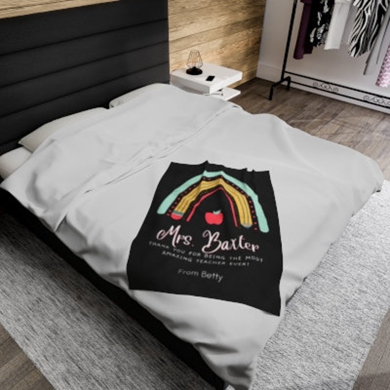 May include: A black and white throw blanket with a rainbow design made of pencils and an apple. The text on the blanket reads "Mrs. Baxter Thank you for being the most amazing teacher ever! From Betty".