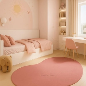 May include: A pink bedroom with a bed, desk, and a large, kidney-shaped rug. The walls are painted a soft pink, with a mural of a sun and birds. A stuffed elephant sits near the bed. The room has a minimalist design.