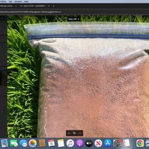 May include: A close-up of a clear plastic bag filled with a brown, granular substance. The bag is lying on a bed of green grass.