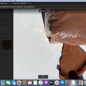 May include: A close-up of a brown powder in a clear plastic bag. The bag is partially open and some of the powder has spilled out onto a white surface.