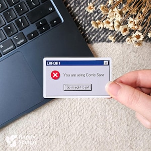 May include: A white sticker with a blue border, resembling a computer error message. The sticker reads "ERROR!" with a red "X" and the text "You are using Comic Sans." Below, it says "Go straight to jail."