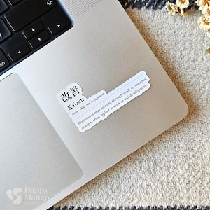 May include: A white sticker with black text on a silver laptop. The sticker says "改善 Kaizen noun /Kai-zen/ Japanese Continuous improvement through small, incremental changes, often applied in work or self-development."