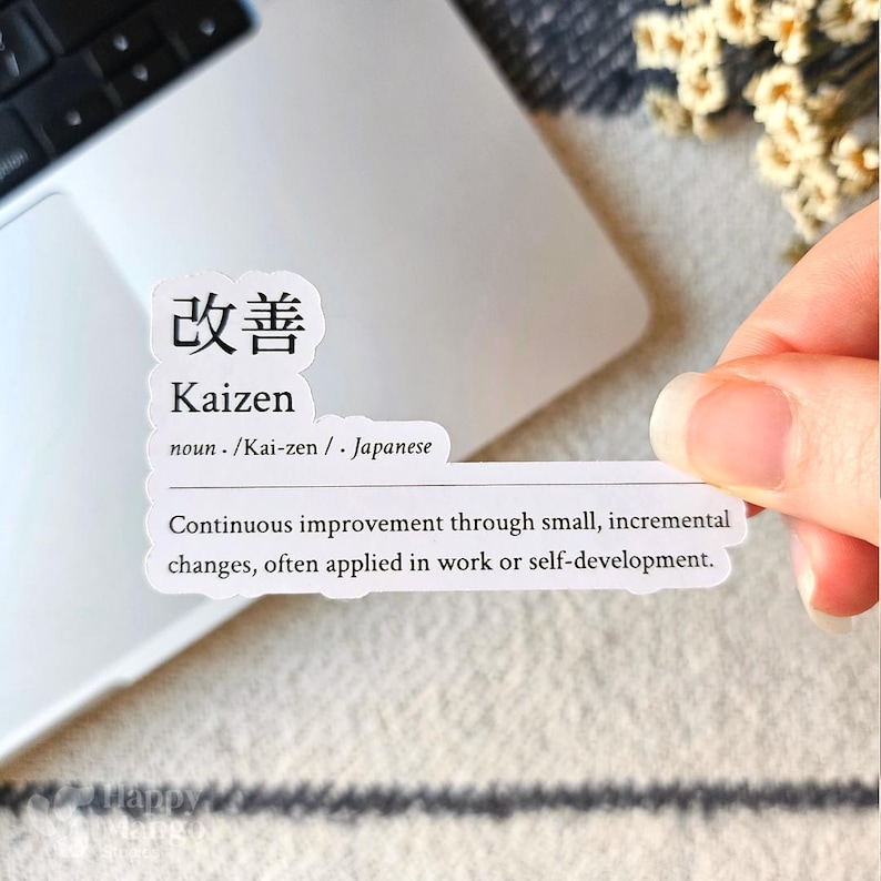 May include: A white sticker with black text that reads "改善 Kaizen noun /Kai-zen/ Japanese Continuous improvement through small, incremental changes, often applied in work or self-development."