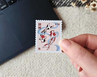 May include: A postage stamp featuring two koi fish in a flowing design with blue accents. The stamp has Japanese text and a value of ¥50. The background is a light pink color.