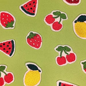 Può includere: Toppe di frutta ricamate tra cui fette di anguria, fragole, ciliegie e limoni su sfondo verde chiaro. Le toppe hanno bordi bianchi e sono realizzate con filo colorato.