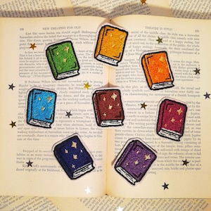 Op de afbeelding: Set van tien geborduurde strijklabels met kleurrijke boeken met gouden sterren. De boeken zijn in verschillende kleuren, waaronder groen, blauw, rood, oranje en paars.