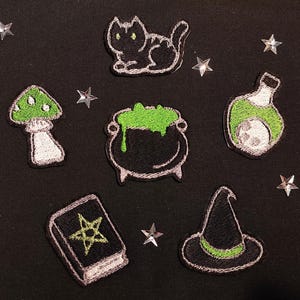 Peut inclure: Un ensemble de neuf patchs thermocollants représentant un chat noir, un champignon vert, un chaudron avec un liquide vert, une fiole de potion verte, un livre avec un pentagramme, un chapeau de sorcière et trois étoiles argentées.