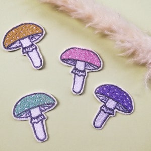 May include: Four embroidered mushroom patches in different colors: yellow, pink, green, and purple. Each patch features a white stem and white spots on the cap.
