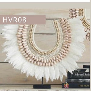 May include: A white feather and shell necklace with a wooden bead accent. The necklace is displayed on a black stand.