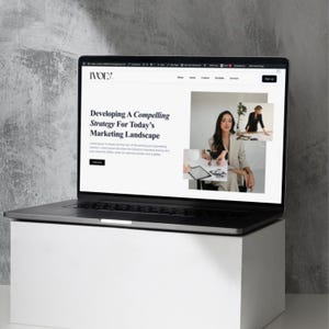 May include: A black laptop displaying a website with the text "Developing A Compelling Strategy For Today's Marketing Landscape." The laptop is on a white box against a gray background. The website features images of a woman in a blazer.