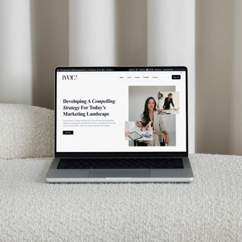 May include: A silver laptop displaying a website with the text "Developing A Compelling Strategy For Today's Marketing Landscape." The website features images of a woman in a blazer and a woman working at a table. The laptop is on a white, textured surface.