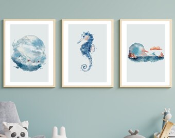 以下が含まれることがあります： 3つの額入り水彩画プリント。プリントは、渦巻く雲の形成、タツノオトシゴ、海岸の風景など、海をテーマにしたイラストを特徴としています。アートワークは青色で、明るい木製のフレームが付いています。淡い青色の壁に飾られています。