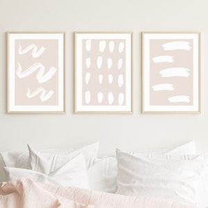 Puede incluir: Tres impresiones de arte abstracto enmarcadas con un fondo rosa pálido y pinceladas blancas. Las impresiones presentan diferentes diseños abstractos, que incluyen líneas onduladas, puntos y líneas horizontales.