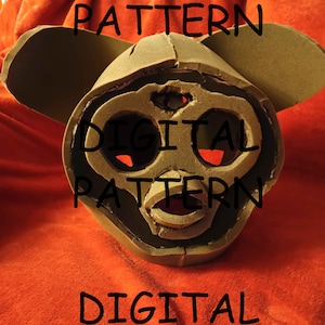 Pode incluir: Uma máscara de espuma castanha com orelhas grandes e traços faciais, sobre um fundo vermelho. O texto "DIGITAL PATTERN" é repetido várias vezes na imagem.