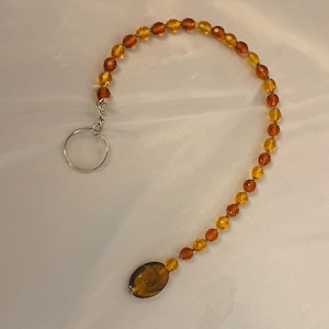 May include: A beaded keychain with amber and yellow faceted beads. The beads are strung together with a silver-coloured metal ring and a decorative oval bead at the end. The beads transition in colour from amber to yellow.