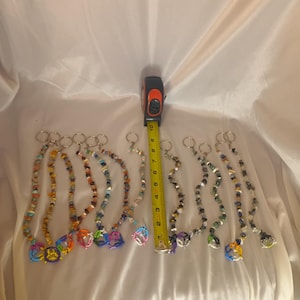 May include: A selection of beaded keychains in diverse colours and designs. The keychains feature colourful beads and charms. A measuring tape indicates the keychains are about 15 cm in length.