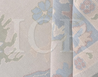 May include: Close-up of a rolled-up rug with a floral pattern. The rug features a cream-colored background with light blue, pink, and green floral designs. The edges are bordered with a light blue and cream pattern.