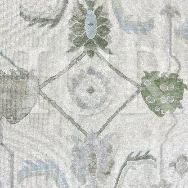 May include: Close-up of a cream-colored rug with a detailed floral pattern. The design features stylized flowers and geometric shapes in shades of green, blue, and gray. The rug has a textured appearance, suggesting a woven construction.