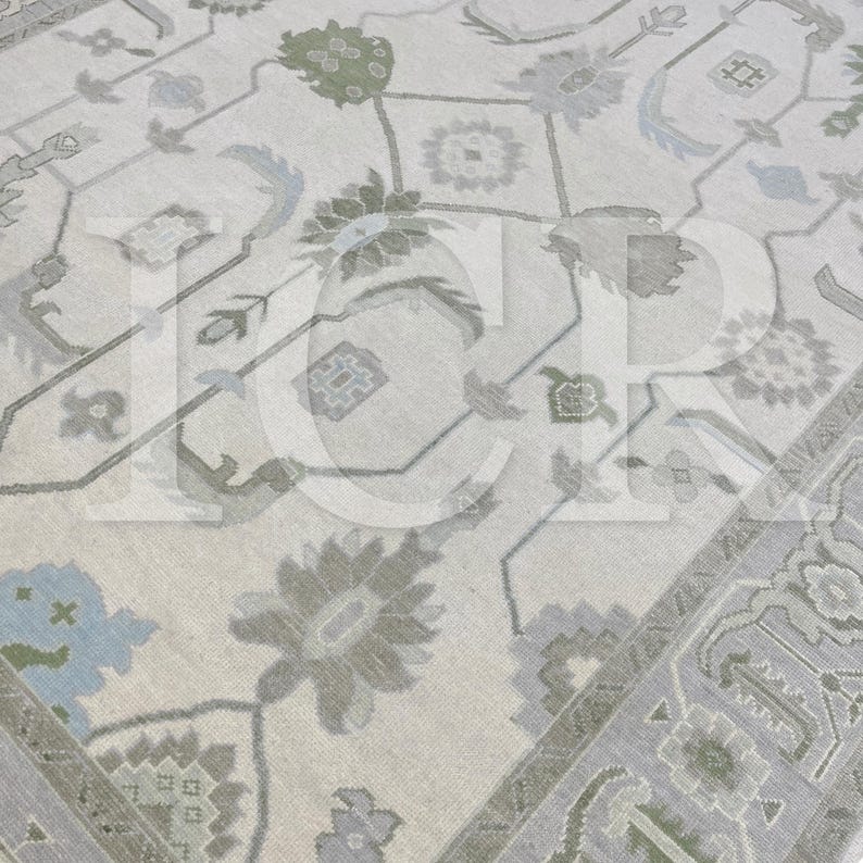 May include: A detailed close-up of a beige area rug with an intricate floral and geometric pattern. The rug features muted tones of gray, green, and blue, creating a soft, inviting aesthetic. The design includes stylized flowers and repeating shapes.