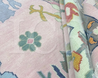 May include: A close-up of a pink rug with a floral pattern. The rug features a repeating design of flowers and other shapes in shades of pink, blue, green, and yellow. The rug is folded over in the image.