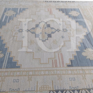 May include: A large area rug featuring a central geometric diamond motif in shades of blue, beige, and cream. The design includes intricate border patterns and symmetrical floral-inspired elements, with the letters ICP overlaid in white.