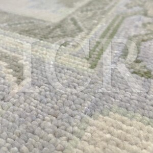 May include: Close-up of a textured rug with a soft, plush appearance. The rug features a subtle pattern in shades of light green, gray, and cream. The design is slightly blurred, suggesting a focus on the texture and color variations.