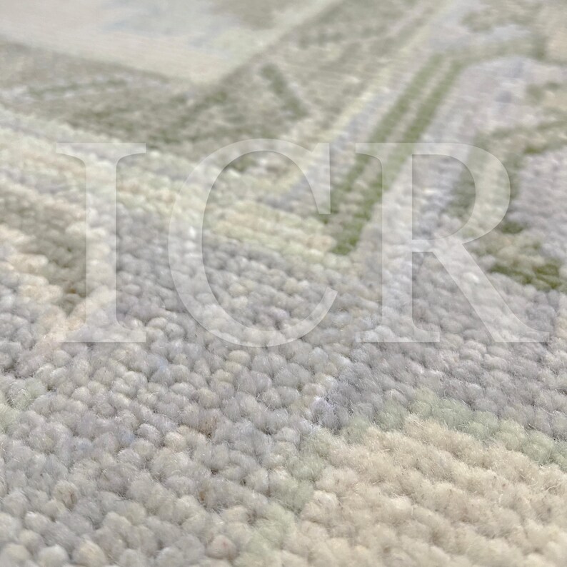May include: Close-up of a textured rug with a soft, plush appearance. The rug features a subtle pattern in shades of light green, gray, and cream. The design is slightly blurred, suggesting a focus on the texture and color variations.