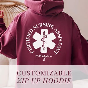 May include: Burgundy zip-up hoodie with a white graphic of a medical symbol and the text "CERTIFIED NURSING ASSISTANT" and a name "morgan".  The hoodie is customizable.