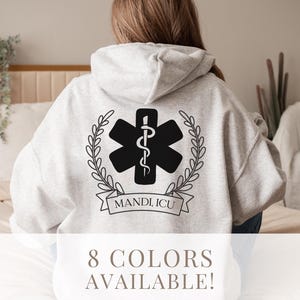 May include: A grey hooded sweatshirt with a black medical symbol, a wreath, and the text "MANDI, ICU" on the back.