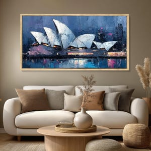 May include: An abstract painting of the Sydney Opera House in Australia. The artwork features the iconic white sails against a dark blue sky, with reflections in the water below. The painting is framed in a light wood.