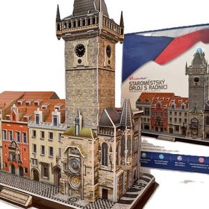 Puede incluir: Un modelo detallado de la torre del Reloj Astronómico de Praga, con una esfera de reloj, detalles arquitectónicos y una fachada multicolor. El modelo va acompañado de una caja con la bandera checa y el nombre del producto.