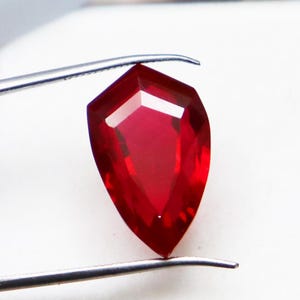 May include: A deep red pear-shaped gemstone with a faceted cut.