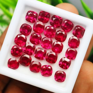 May include: A collection of 20 loose, vibrant red gemstones in a square cushion cut. The gemstones are displayed in a white tray.