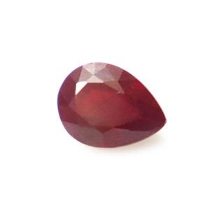May include: A pear-shaped, faceted gemstone with a deep, saturated red colour. The stone features a pointed end and a rounded base, with multiple triangular and kite-shaped facets cut into its surface to reflect light across its dark red body.